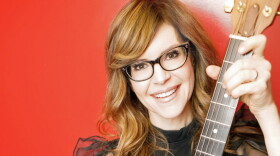 Woman with reddish blonde hair holding up a guitar 