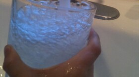 A person holding a glass under a running faucet.