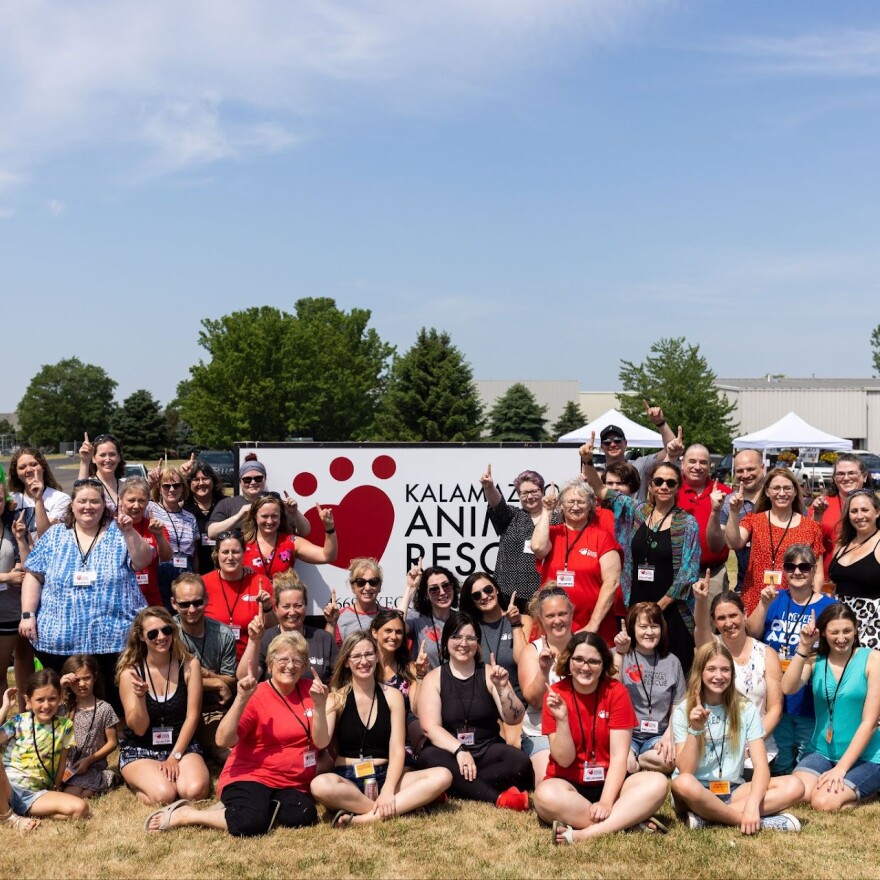 Kalamazoo Animal Rescue volunteers and staff, index fingers raised to signify "until every 1 has a home"