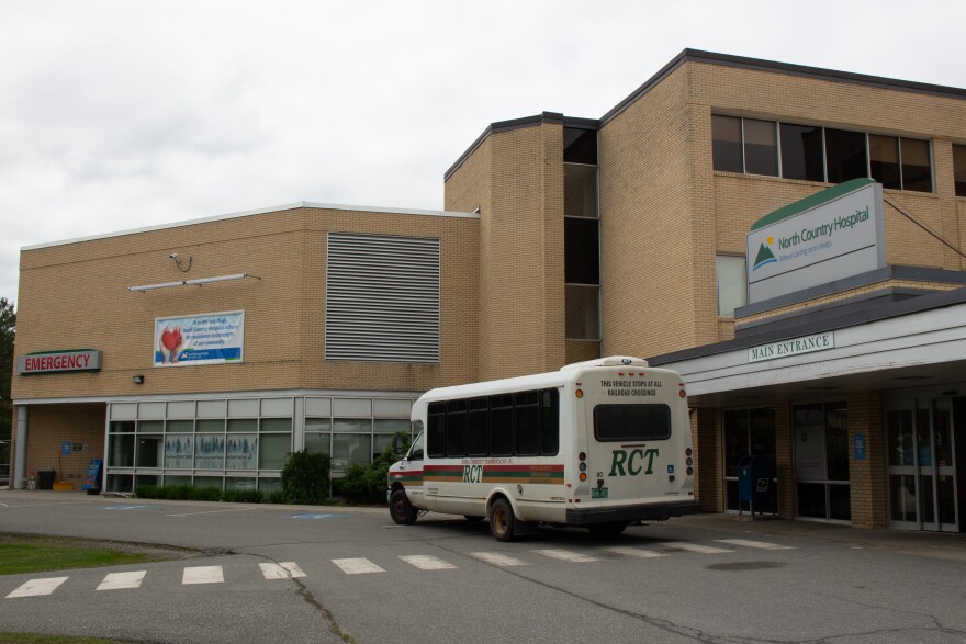 A bus with the lettering RCT sits outside a light-brown brick building with a sign on the right that reads "North Country Hospital" and another on the far left that reads "Emergency."