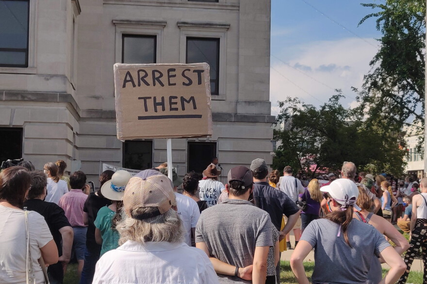 A demonstrator holds a sign calling for the arrest of a group of White people who assaulted a Black man while shouting racial slurs on July 4.