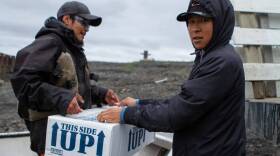 Two men in jackets lift a box that says "This side up"