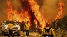 Flames from the LNU Lightning Complex fire leap above a road Sunday as firefighters work to contain the blaze in Lake County, Calif.