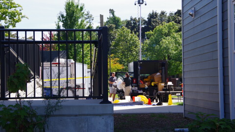 Two individuals can be seen holding a large, plastic object near several trailers in a building parking lot.