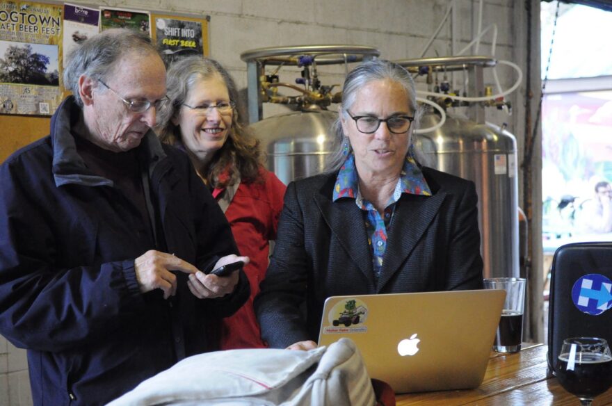 Helen Warren (right) shows two guests the election voting results on the Alachua County Supervisor of Elections website while hanging out at First Magnitude Brewery in Gainesville. Phones and computers were constantly refreshed throughout the night to keep up-to-date on new voting results. (Baylor Cherry/WUFT News)