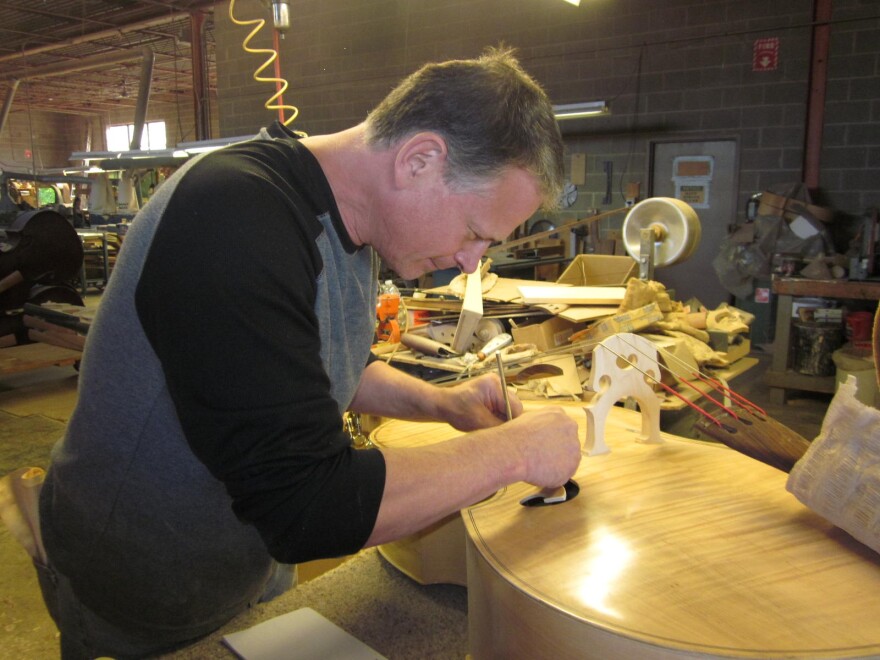 Tom Link, owner of Link Bass and Cello, glues a label into a finished bass violin in his factory.