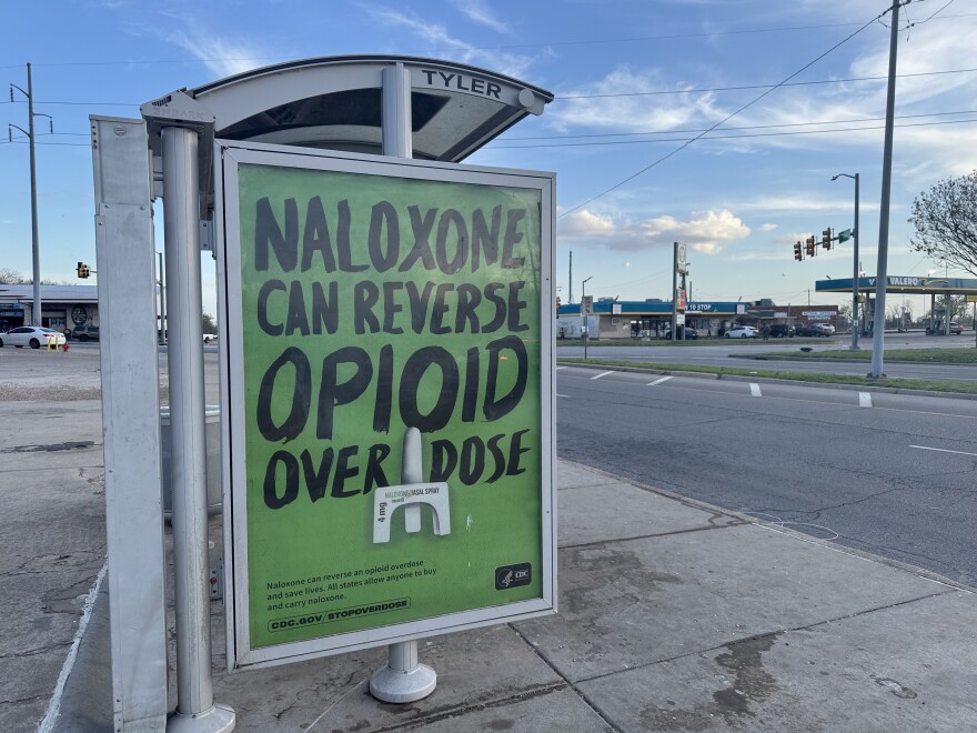 A CDC sign about naloxone, an overdose-reversing medication, hangs on the side of a bus stop in Oklahoma City.