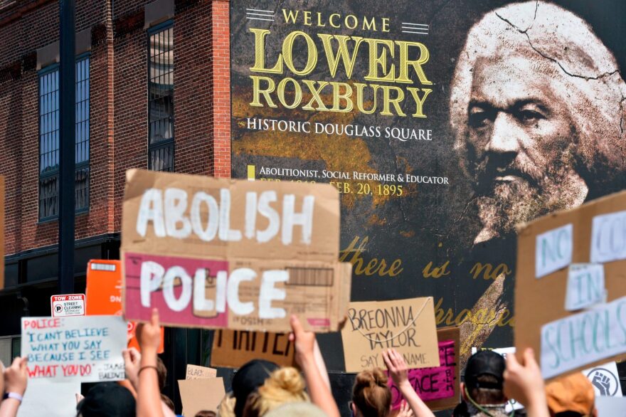 Protesters march by a photo of Frederick Douglas, a historic abolitionist, during a Juneteenth protest and march in honor of Rayshard Brooks and other victims of police violence in Boston, Massachusetts. Abolitionists advocate for a world without prisons or police. 