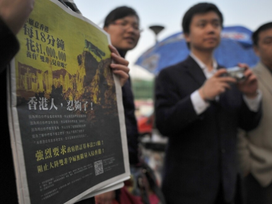 A girl holds a Hong Kong newspaper with an anti-mainland Chinese advertisement featuring a picture of a locust looking over the Hong Kong cityscape. The ad is one of the latest signs of Hong Kong fears that mainlanders are overrunning the territory.