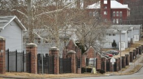 A row of gray apartments sit behind black, wrought iron fencing.