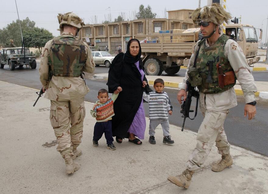 An Iraqi woman holds the hand of two children as she walks past two U.S. soldiers after they briefly stopped a vehicle at an intersection in downtown Tikrit, north of Baghdad, on Nov. 10, 2003.