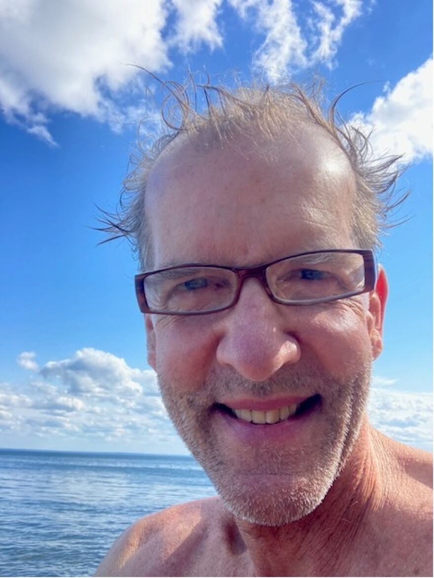 Close-up of a man next to a large body of water; man looks as though he just got done swimming