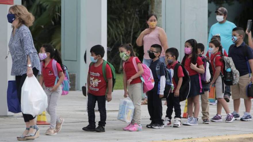 First-graders at Redland Elementary in Homestead are led into the classroom by their teacher after being dropped off by their parents on Oct. 5, 2020. It’s the first day of school reopenings for in-person classes at Miami-Dade County Public Schools. On Monday, only students in pre-K, kindergarten and first grade, plus students with disabilities, were welcomed back to schools; other students will return on Wednesday and Friday.