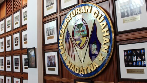 A wall filled with multiple framed pictures, each contributing to a Guam legislature's history.
