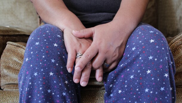A Nicaraguan woman, above, and her family came to the United States from Costa Rica after experiencing violence in there. They arrived in the Kansas City area in 2024 and are seeking asylum. The woman is sitting on a light brown couch. The photo is cropped so her face is not available. She wears blue pants with red, white and blue stars. Her hands are placed together on her lap.