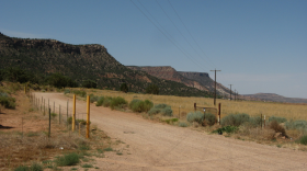 A dirt road near a yellow field with mountains in the near foreground, stretching off into the background.