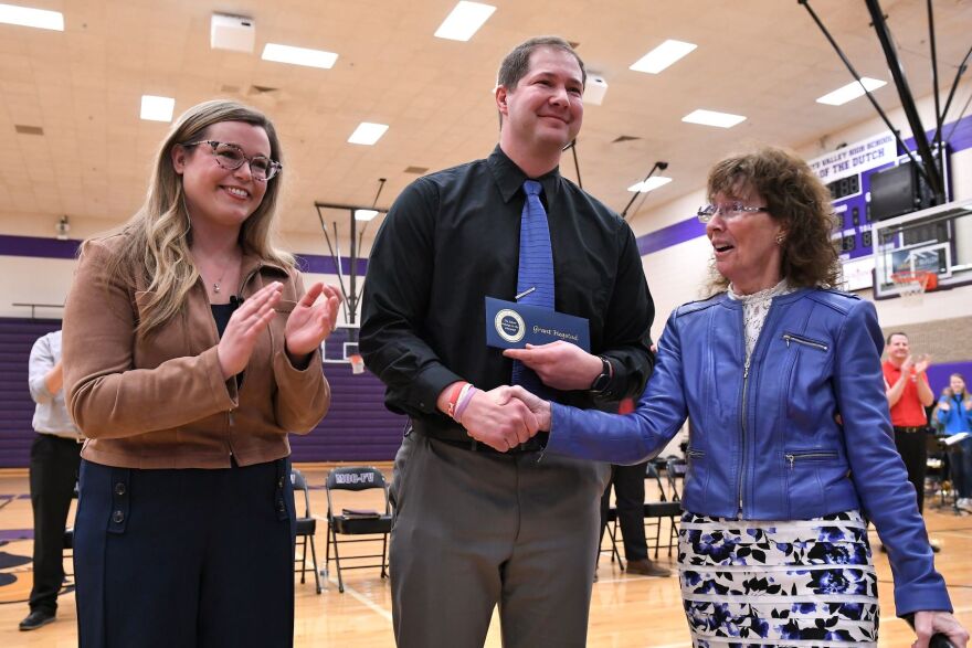 A high school principal wins an award from the Milken Family Foundation. The award ceremony took place at a high school gym.