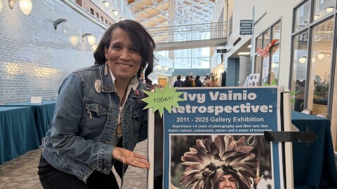 Interior image of a woman standing by a sandwich board promoting an art exhibit