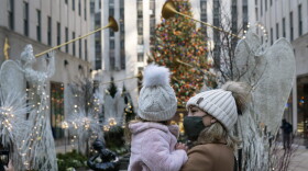 A woman holds her daughter as they look at the Rockefeller Center Christmas Tree, Thursday, Dec. 3, 2020 in New York.  What’s normally a chaotic, crowded tourist hotspot during the holiday season is instead a mask-mandated, time-limited, socially distanced locale due to the coronavirus pandemic.  (Mark Lennihan/AP)