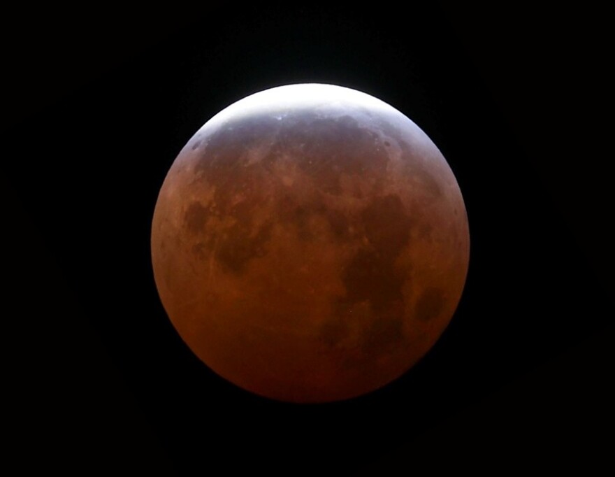 A moon during a lunar eclipse; most of the surface shadowed and red
