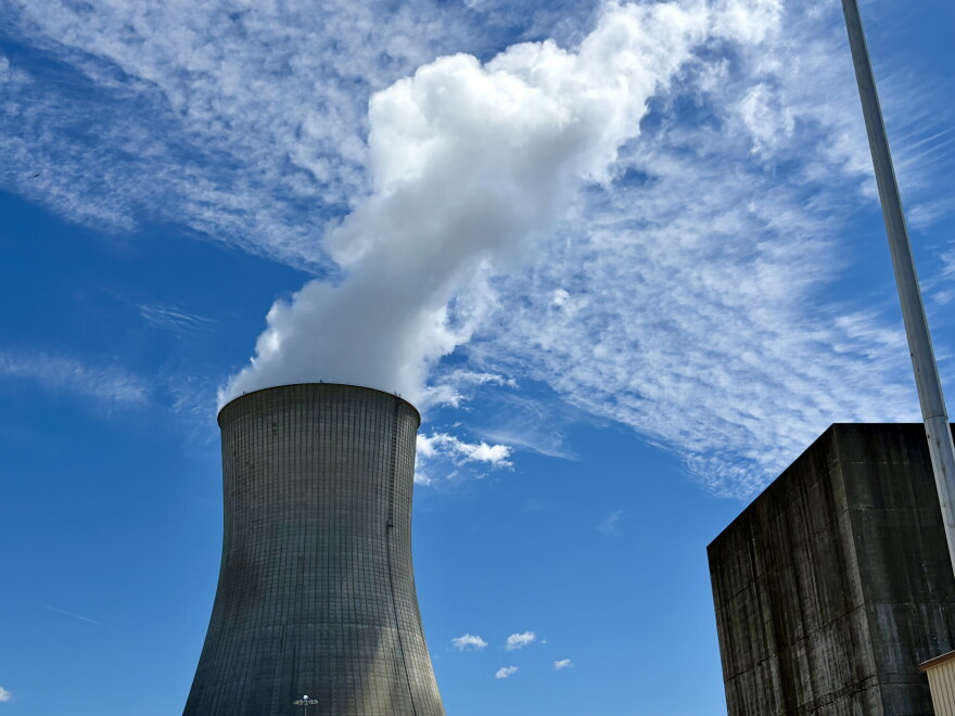 A wide shot of the Callaway Nuclear Power Plant cooling tower. It's wider at the top and bottom and white water vapor comes from the top. The sky is light blue with some slim clouds. 