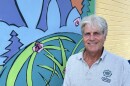 A man wearing a grey polo standing in front of a mural of leaves and forest creatures