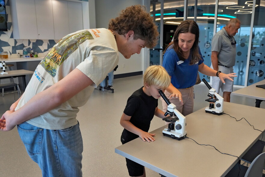 FILE: Staff member Amanda Shuman, second from right, instructs visitors using microscopes in the biomedical and immunology teaching laboratory at the Mote Science Education Aquarium, Monday, Oct. 6, 2025, in Sarasota, Fla.