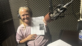 A woman wearing headphones smiles while holding up a copy of Street News.