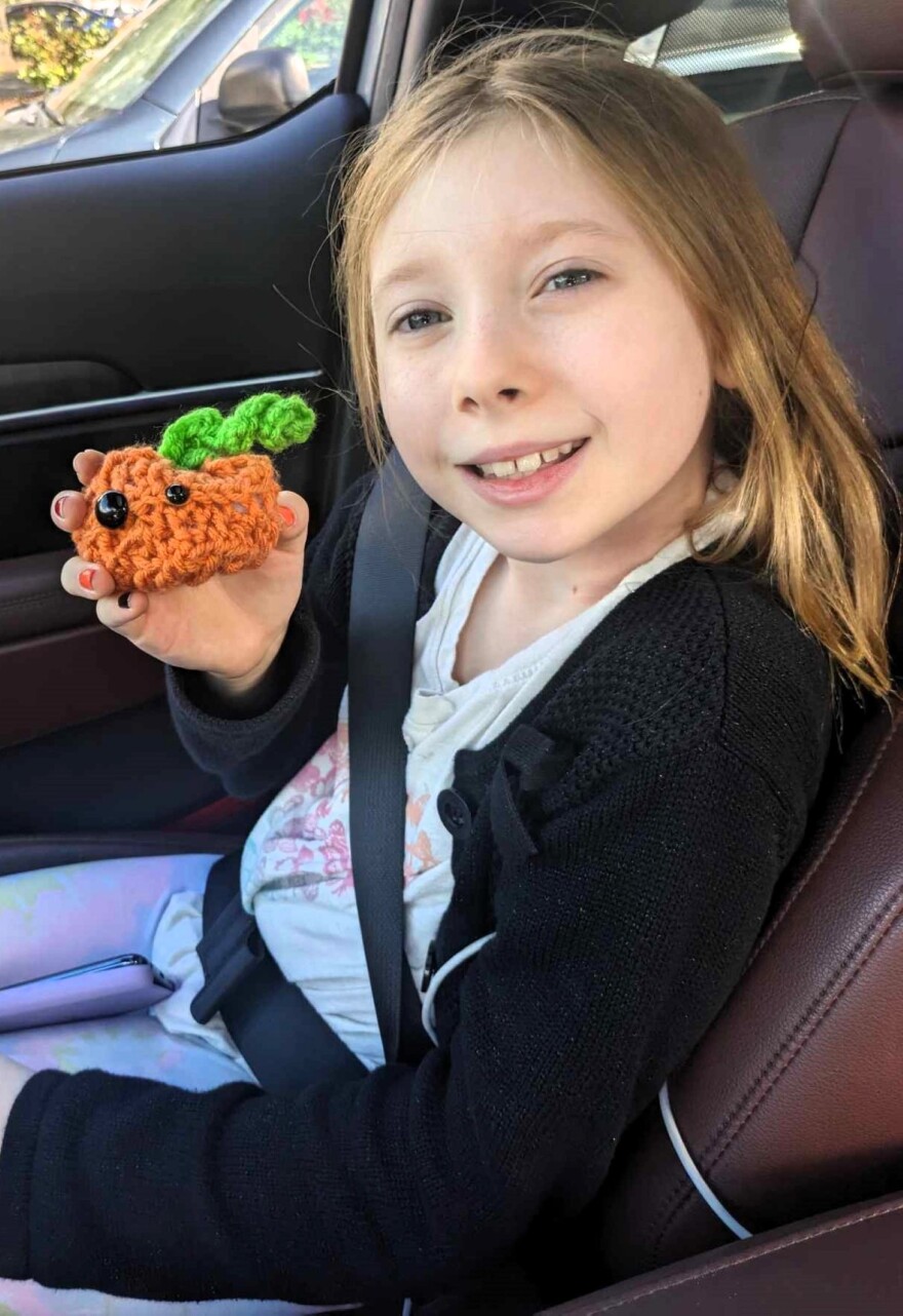 Girl behind a seat belt holding a crocheted craft