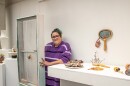 A woman wearing a purple striped shirt stands beside a ceramic installation at SIU’s Sharp Museum, with various colorful ceramic artworks displayed on pedestals and shelves.