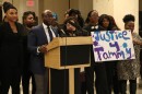 Man speaks at podium. He's surrounded by women, one of which holds a sign that reads, "Justice 4 Tammy."