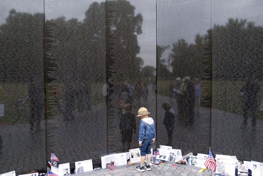 A child reads names etched on the wall at the Vietnam Veterans Memorial, ahead of Memorial Day in Washington, Sunday, May 28, 2023. (AP Photo/Jose Luis Magana)