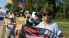 A woman holds an upside-down American flag with the words "America in distress" with other protestors behind her. 
