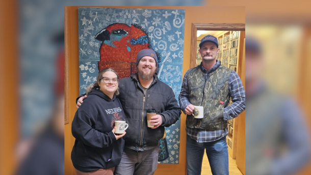Three people stand in front of a painting holding coffee mugs.