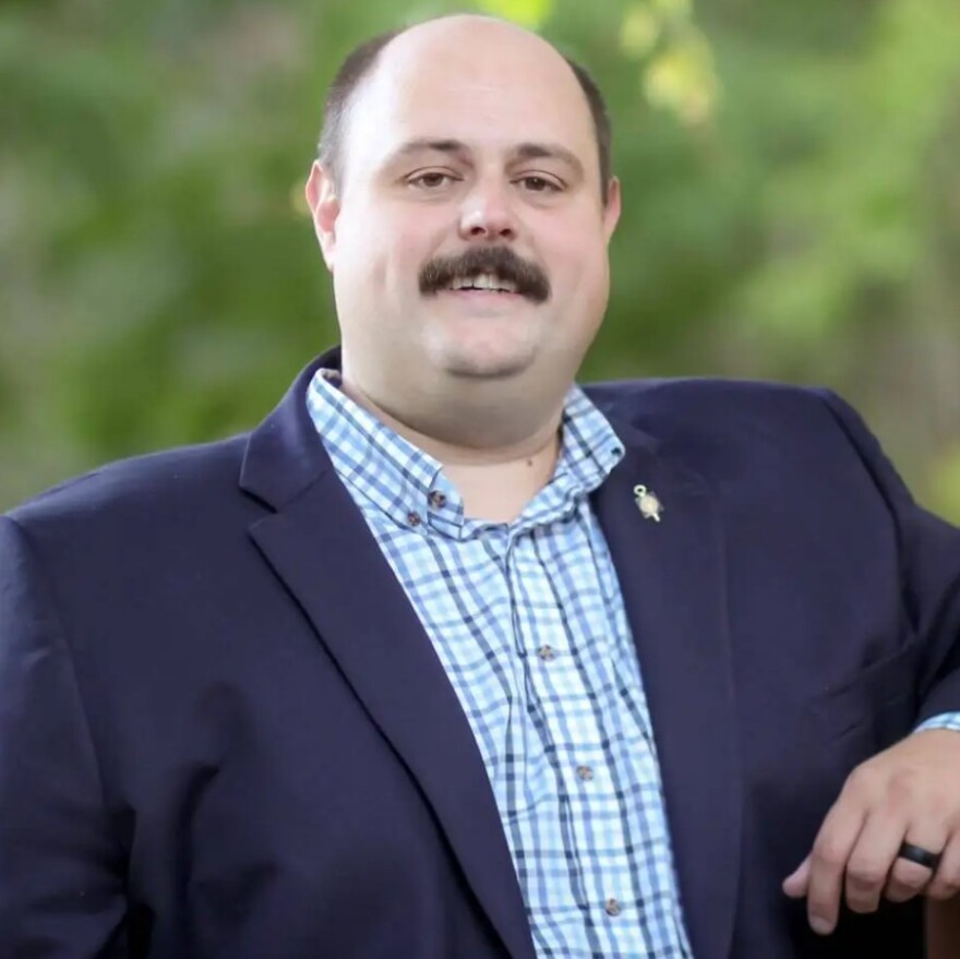 Man with mustache wearing blue blazer standing outside 
