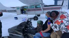 Sarah Lind, a nurse with Yukon-Kuskokwim Health Corp., Southwest Alaska's tribal health care provider, vaccinates James Evan in December, 2020. They're standing on the tarmac in the village of Napakiak, where Evan works for YKHC at the clinic.