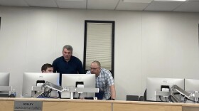 three people look at two computer monitors