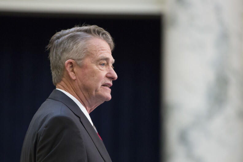 Side profile of Gov. Brad Little standing with a black suit jacket. The background is blurred.