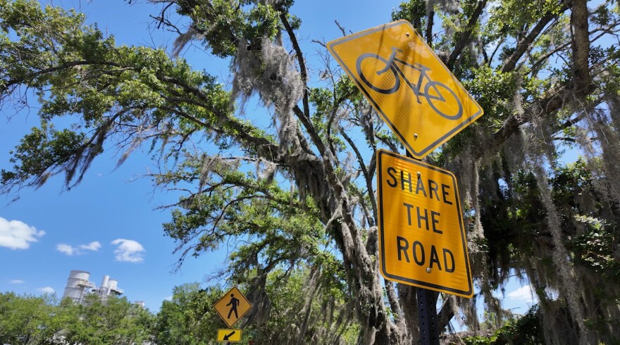A yellow road sign with a bicycle icon reads "Share the Road," advising drivers to watch for bikers 