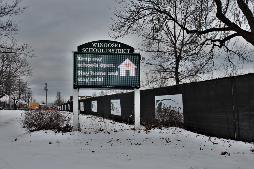 A green lit sign with white letters reads Keep Our Schools Open. Stay home and stay safe.