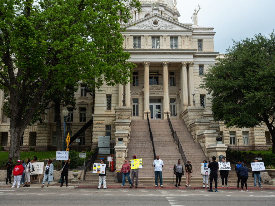 People are standing in a line holding signs outside of a courthouse.