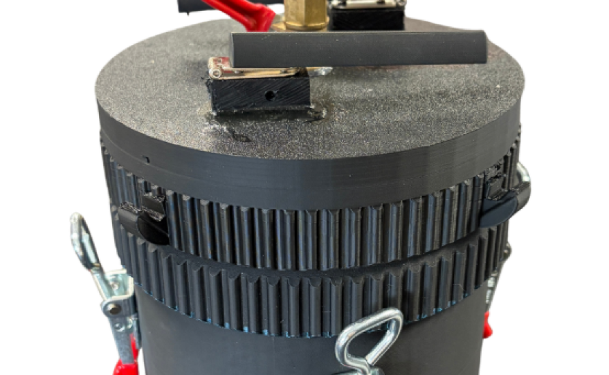 A round black container has silver and red fasteners around the middle and a large bolt on the top.