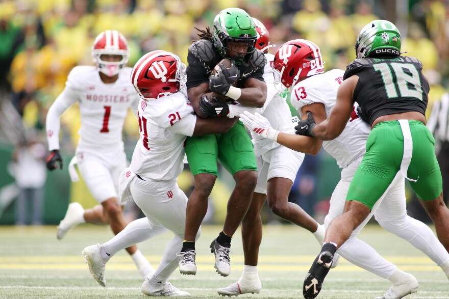 Oregon running back Noah Whittington, center, attempts to break a tackleby Indiana linebacker Rolijah Hardy (21), defensive back D'Angelo Ponds (5) and linebacker Kellan Wyatt (13) during the first half of an NCAA college football game, Saturday, Oct. 11, 2025, in Eugene, Ore.