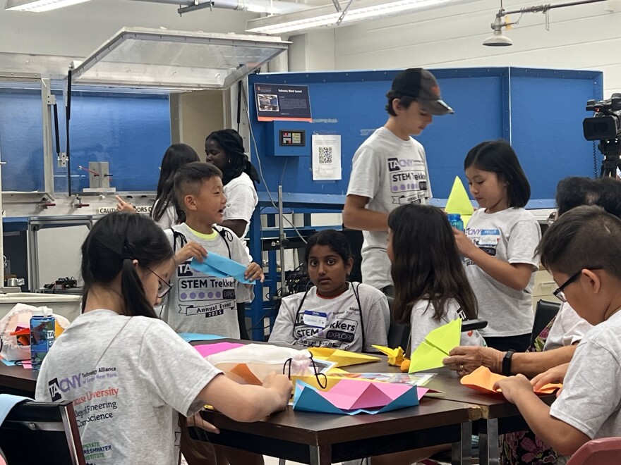 Middle schoolers gather around a work table at Syracuse University's engineering college building aerodynamic paper planes