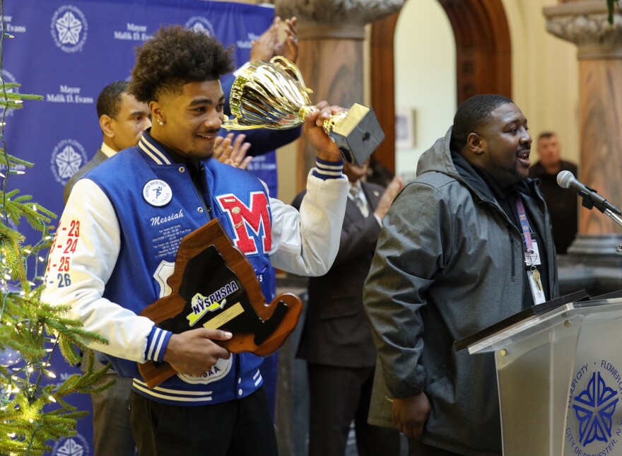 Monroe High School Red Jacket Messiah Hampton holds up the Mayor’s Cup during a formal recognition ceremony at City Hall, where Mayor Malik Evans honored the football team with certificates. The Red Jackets made Rochester City School District history by winning the state championship with a 34–0 victory over Sleepy Hollow, completing a perfect 12–0 season.