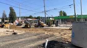 Construction on a major road. Black and yellow machinery is digging up dirt along the road.