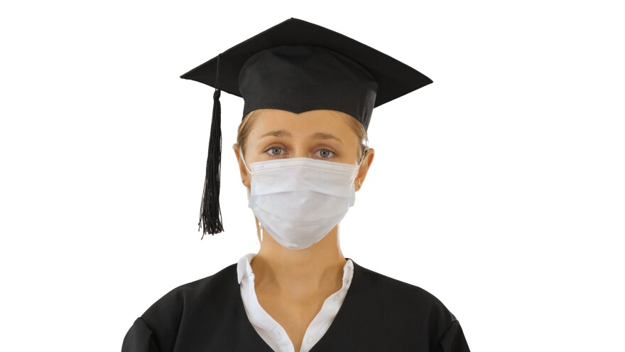 A students wears a cap and gown along with a mask for the pandemic