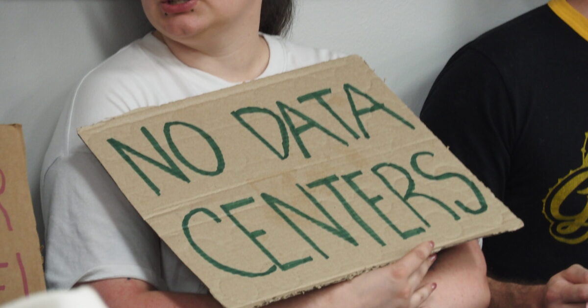 An audience member attending a Pulaski County Quorum Court agenda-setting meeting holds a sign opposing data centers on June