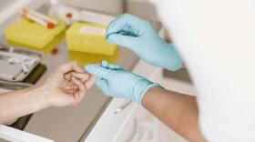 A nurse taking a blood sample from a finger.