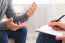 Psychotherapist writing notes, assessing patient's health and giving diagnosis to man sitting on couch during counseling session , panorama, free space.